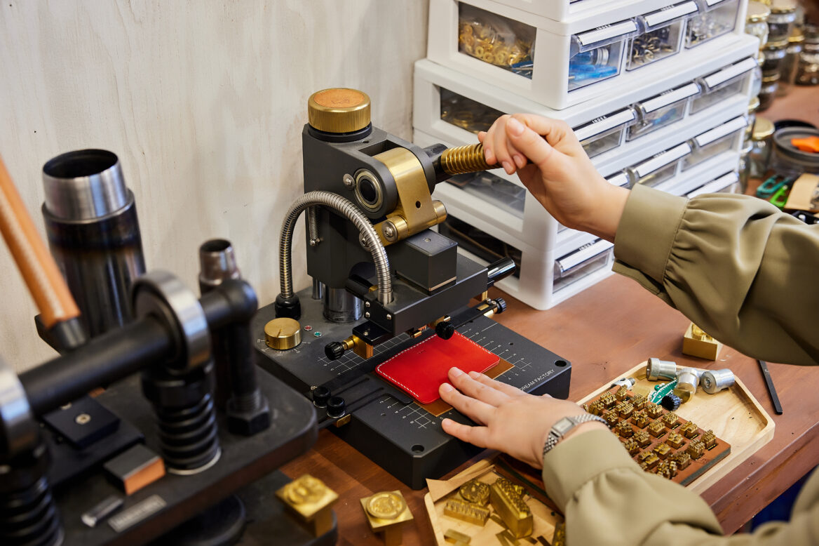 완성된 빨간 카드지갑에 프레스기로 이름 이니셜을 각인하는 사진