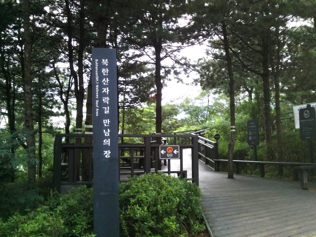 푸릇푸릇한 나무들이 있는 입구에 북한산 자락길 만남의 장 팻말이 있는 모습