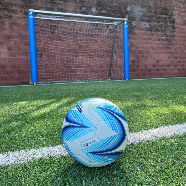 저 멀리 골대가 있고 근접한 거리에 파란색의 축구공이 있는 사진