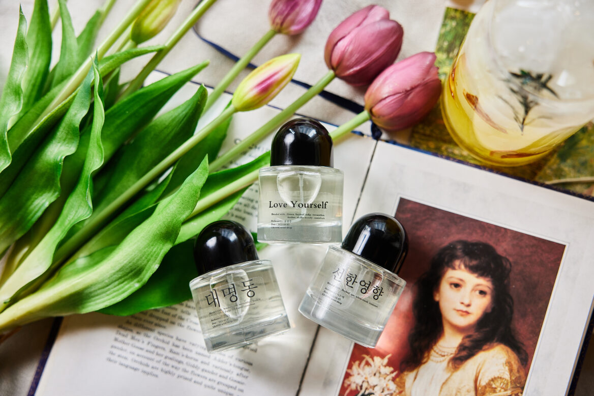 분홍색의 튤립과 잡지위에 투명 용기에 담긴 세 개의 향수가 놓여있는 모습