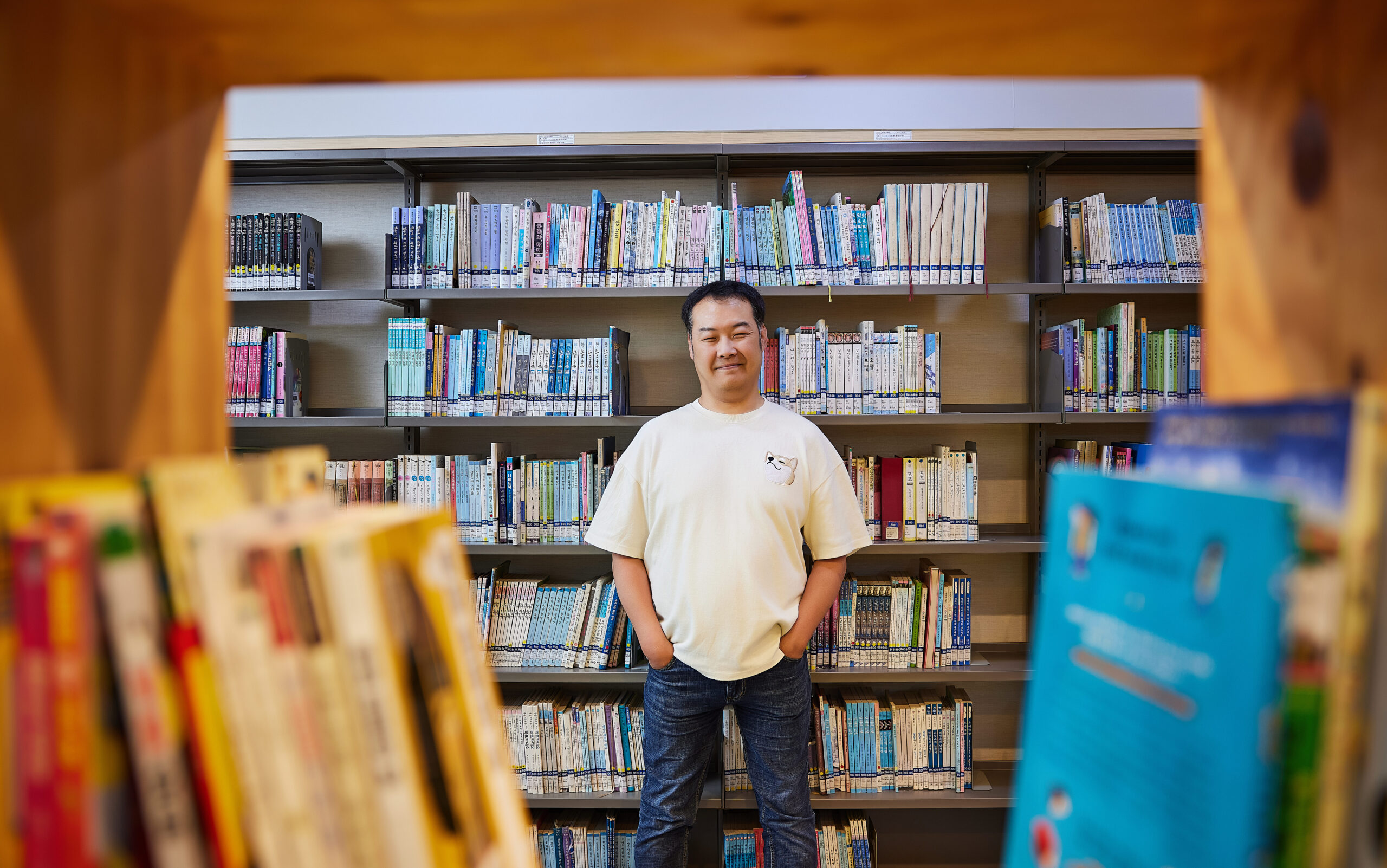 수많은 책을 배경으로 정면을 바라보며 미소짓는 강제길 사서 실무사