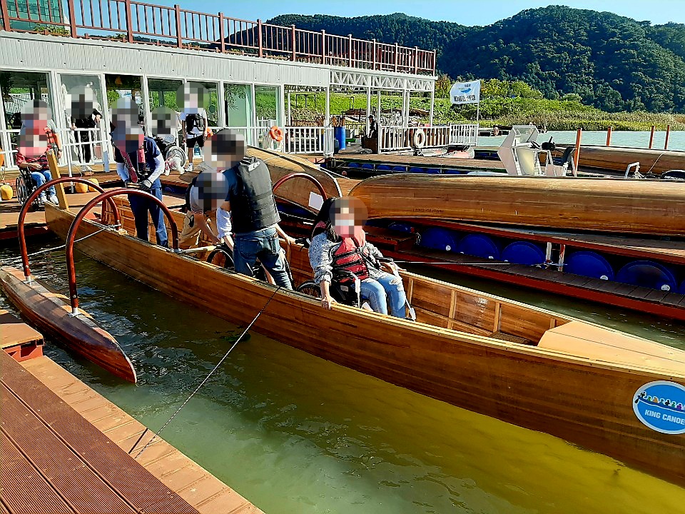 휠체어에 탄 채로 킹카누에 탑승하고 있는 모습의 사진
