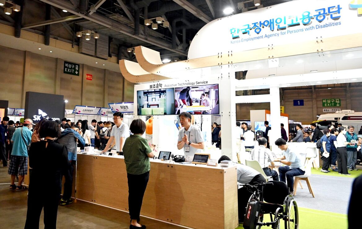 이공이삼 부산세계장애인대회에서 지구촌 장애인들과 함께 장애인고용을 창출하자는 의미의 사진. 사람들이 부스에  모여 있다.