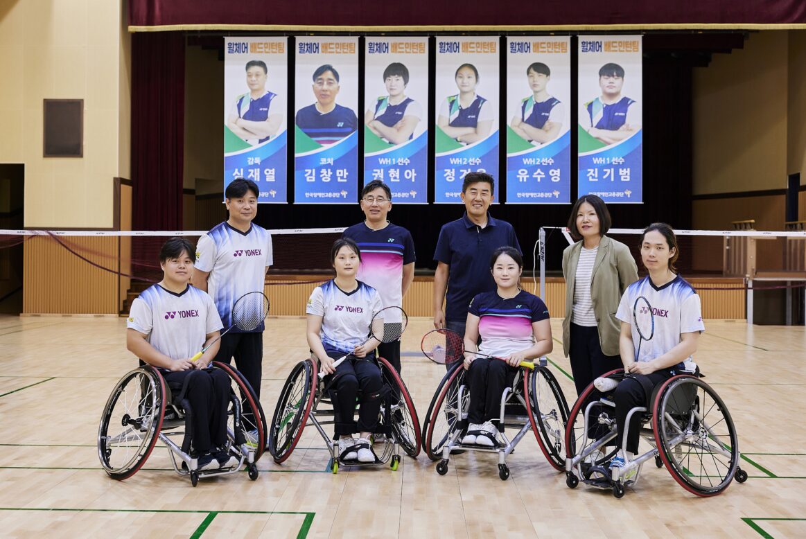 정면을 바라보며 미소를 짓는 한국장애인고용공단 휠체어 배드민턴 선수들과 이들을 지지하는 감독들