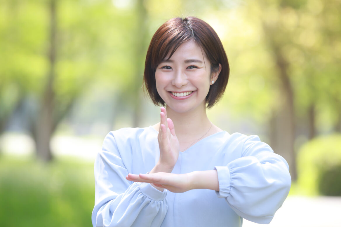 단발머리를 한 여성이 미소를 지으며 감사합니다의 뜻인 수어 동작을 하고 있는 사진